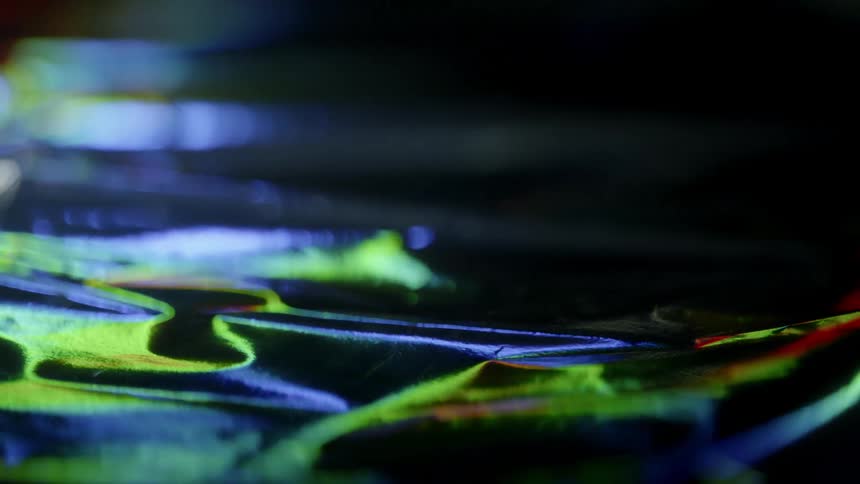 Light, color, and shadow are moving across a reflective surface