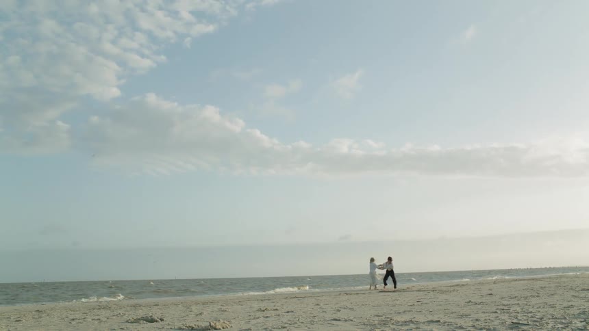 Two children hold hands and spin on a beach