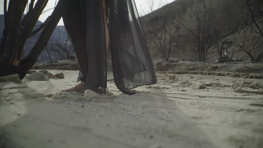 A woman in a black dress stands in the sand
