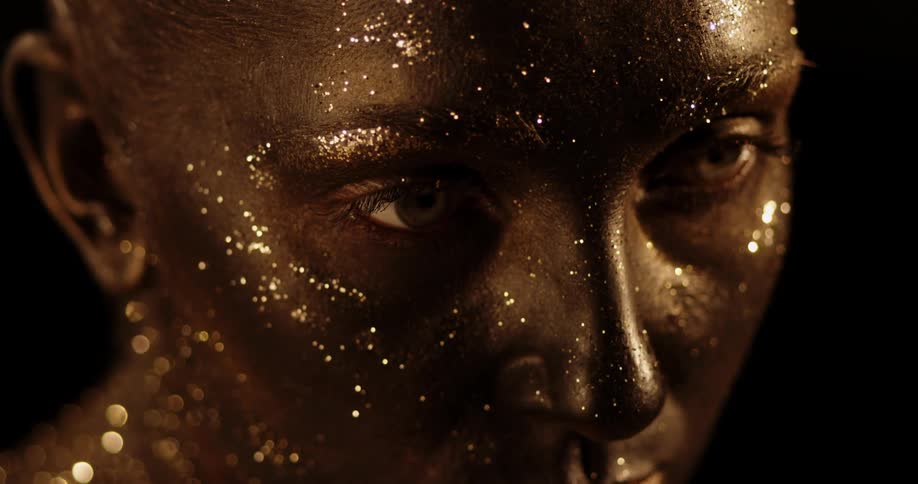 Woman with heavy glitter on her face and neck slowly raises her head and opens her eyes