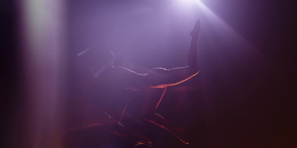 Someone is flipping upside down and holding a pose in a dark room