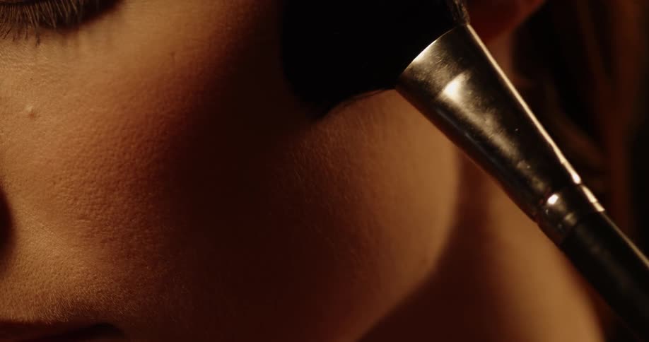 A woman is applying face makeup with a large brush