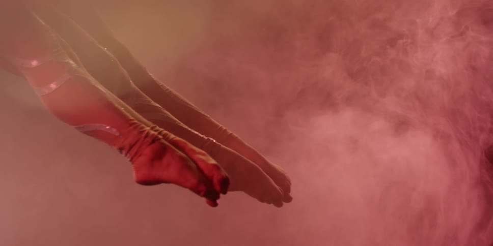 Two women perform aerial acrobatics surrounded by pink smoke