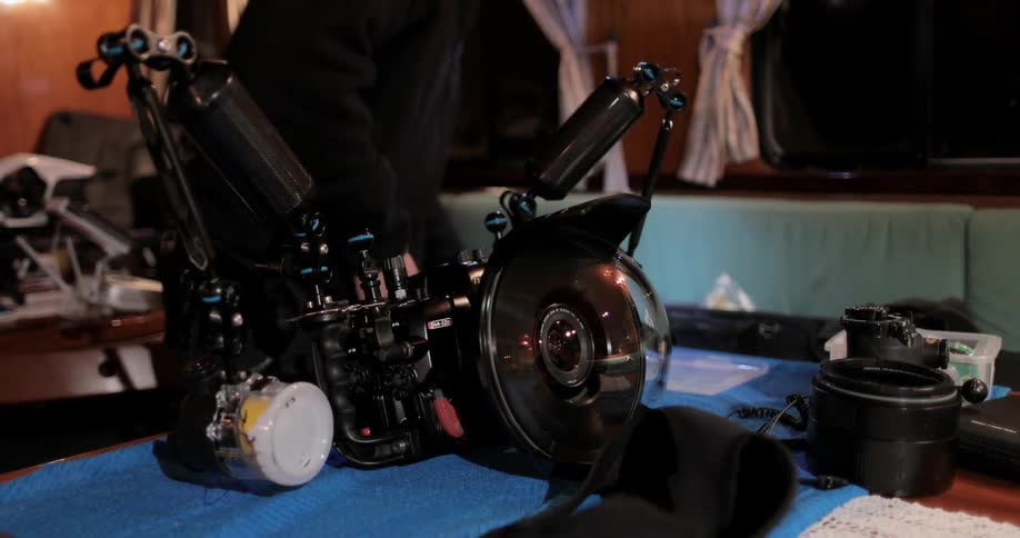 A man is standing inside a boat cabin tending to camera gear at night