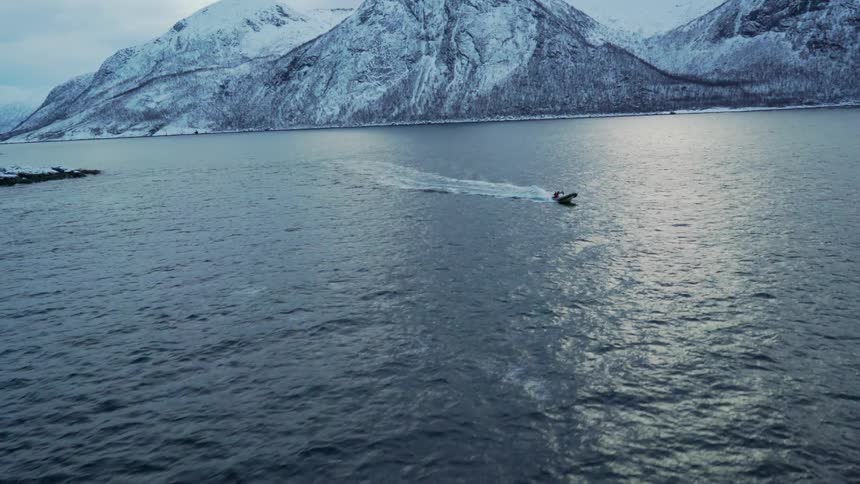 A speed boat sails through the ocean with large snowy mountains in the background