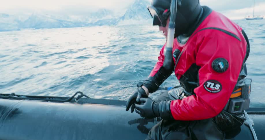 A diver shakes water out of his suit while sitting on a raft