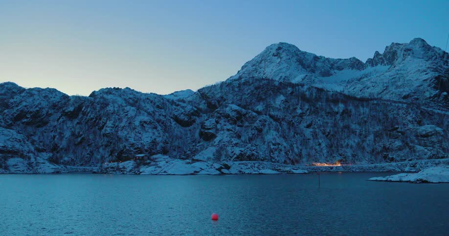 A vehicle is driving on a coastal road past snow-covered mountains at dawn