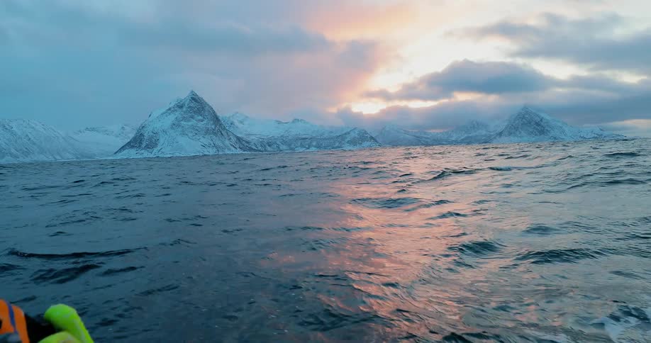 A person reaches off a boat into the ocean waves near the snow covered coast