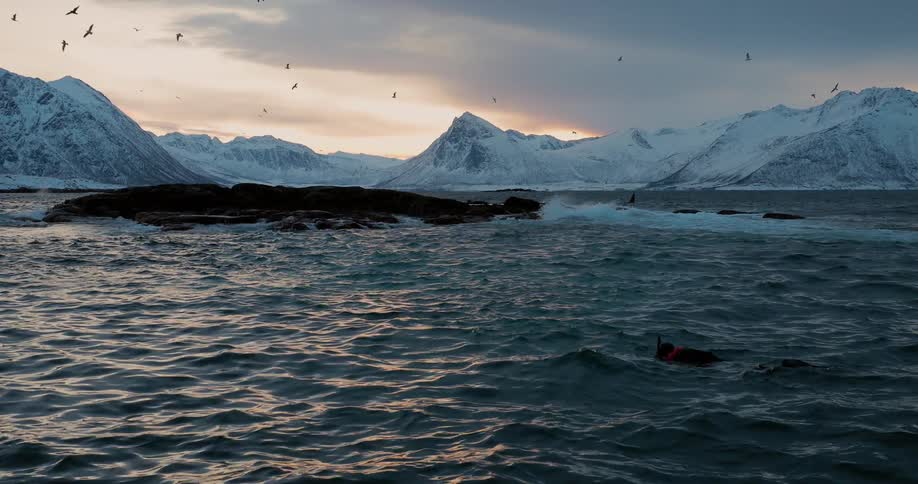 Water crashes into a snowy shoreline at sunset