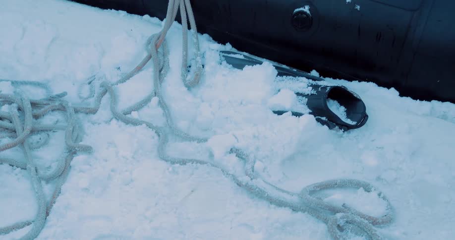 Snow is covering a diving fin and some rope next to a rubber dinghy during the day