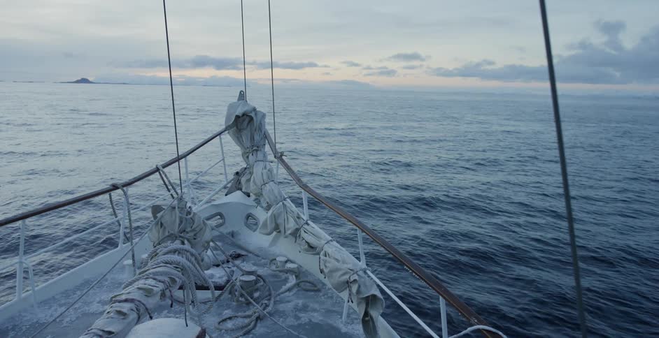 A sail boat is headed towards the horizon at sunset