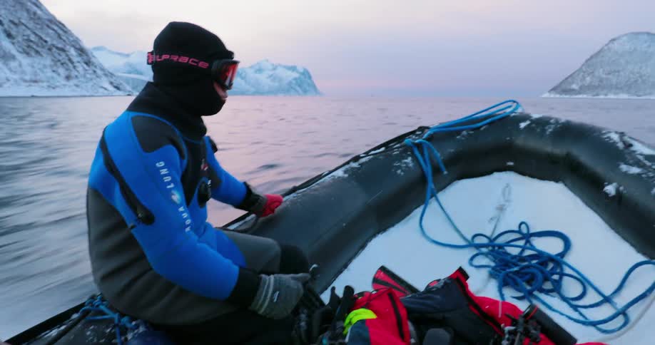 A man is bounced up and down as he rides in a dinghy near a snow-covered coastline
