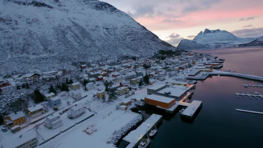 A pier extends from a small town at the foot of a snow covered mountain