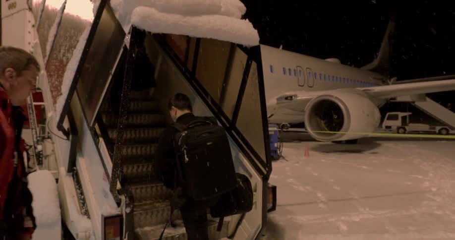 Two men board an airplane while it snows