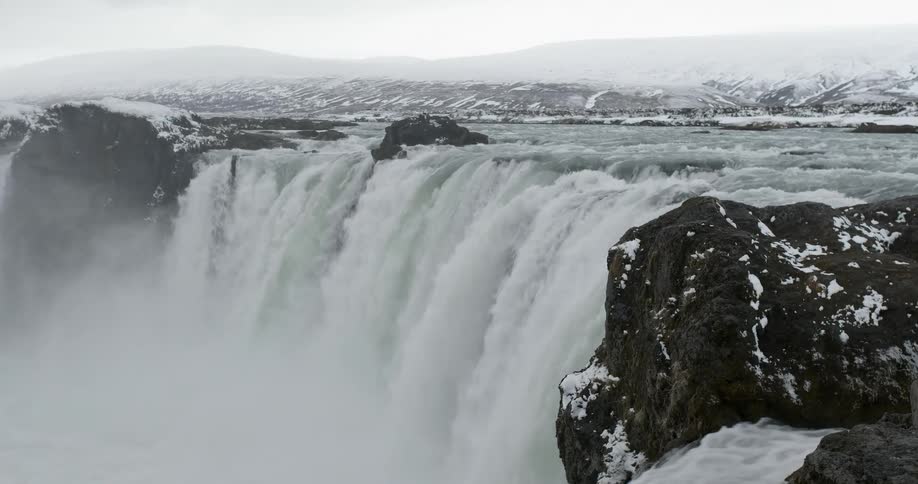 A waterfall flows over a snowy cliff