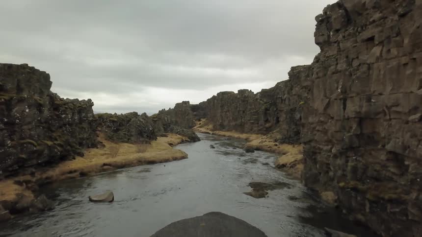 A river flows by rocky cliffs on a cloudy day