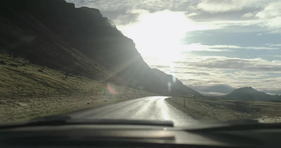 A vehicle is driving on a road through a remote area on a cloudy day
