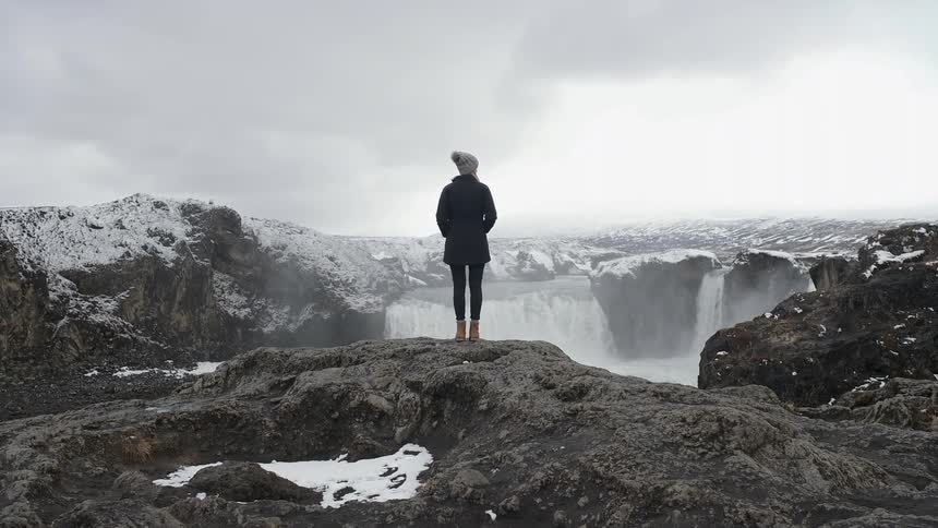 A hiker watches a waterfall in snowy mountains