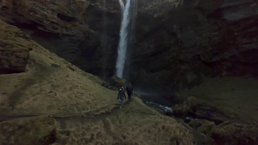 Two people walk towards the base of a waterfall