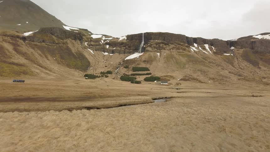A waterfall is cascading over a cliff into a valley during the day