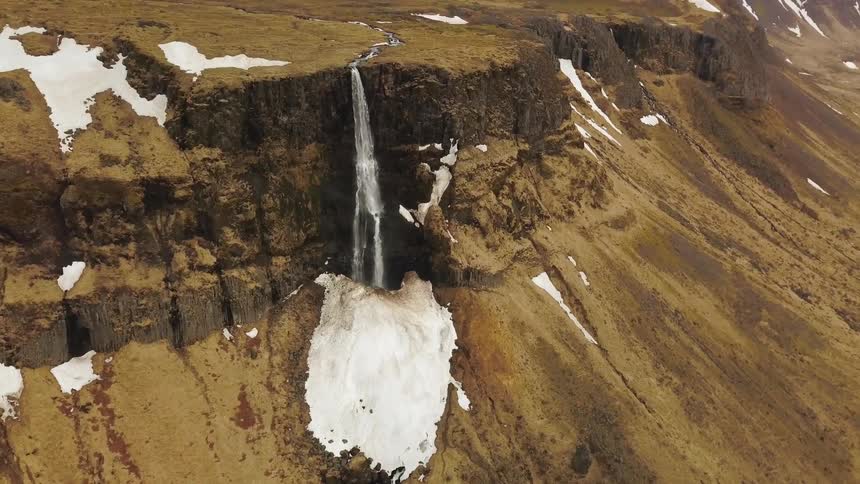 A waterfall flows over a snowy cliff