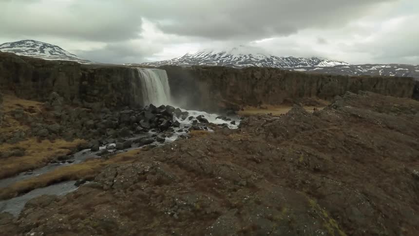 A river gushes over a waterfall near snowy mountains