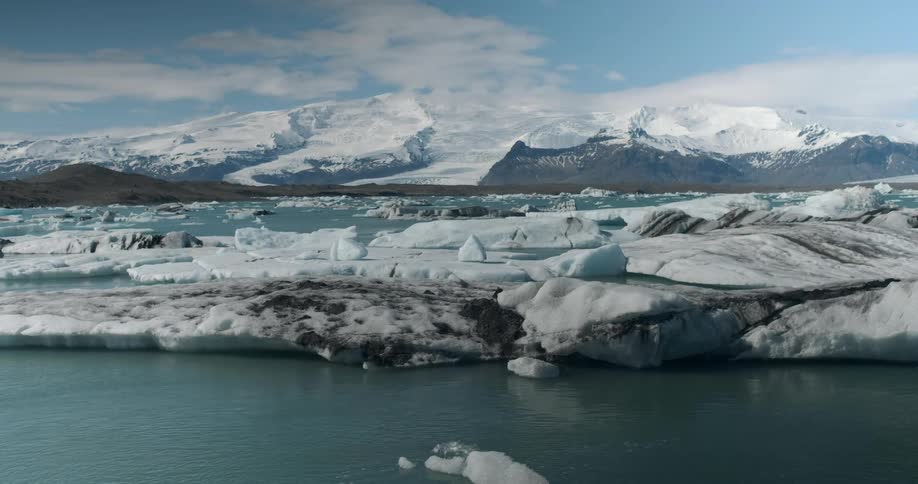 A large piece of ice floats in the water near the snow covered hills