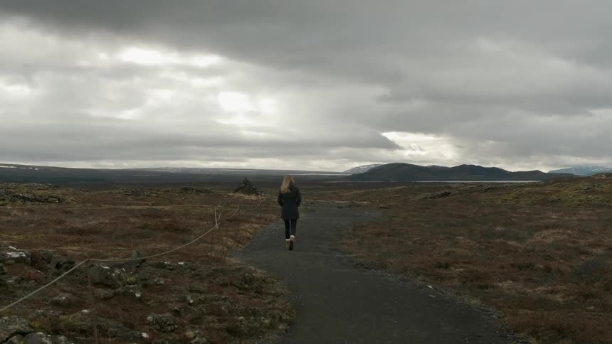 A woman is walking on a path in a remote area on a cloudy day