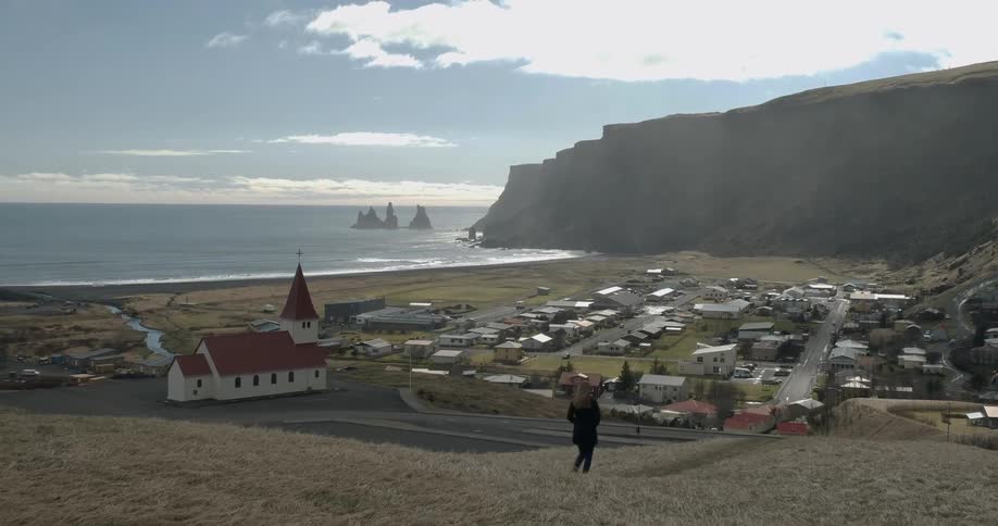 Woman walks down hill towards vik Iceland