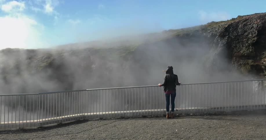 A person stands at a railing as mist flies by in the breeze