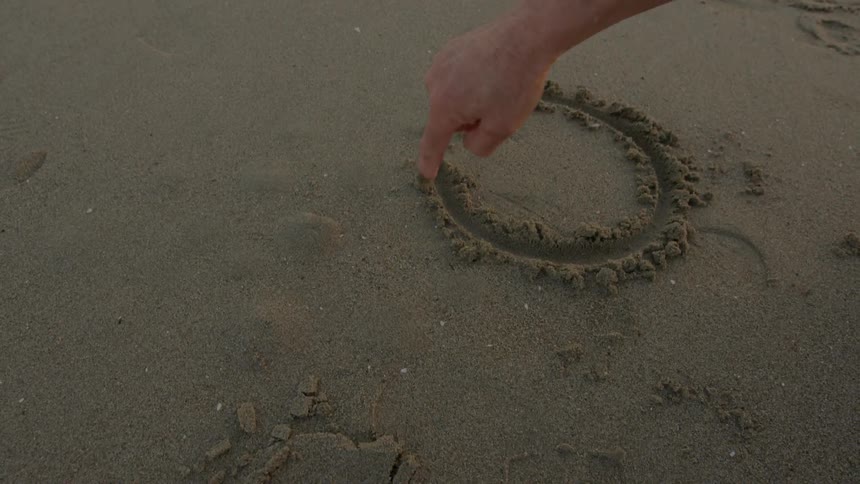 A man writes in the sand with his finger