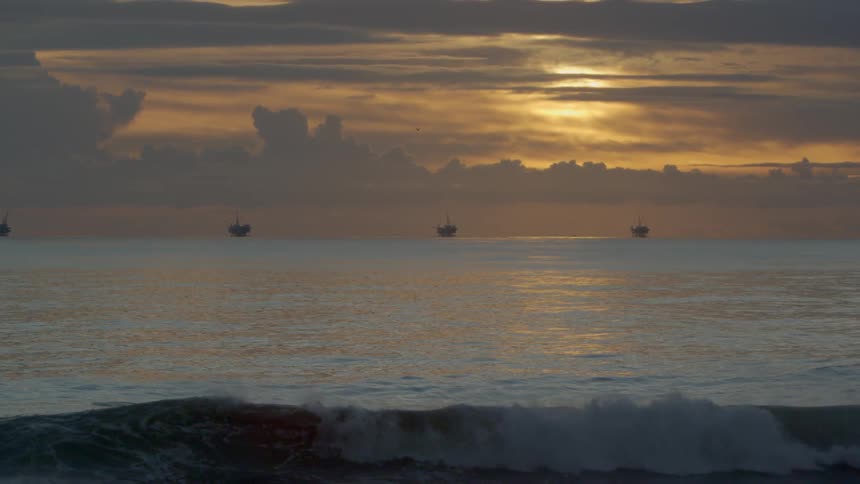 A beach with ships in the distance at sunset