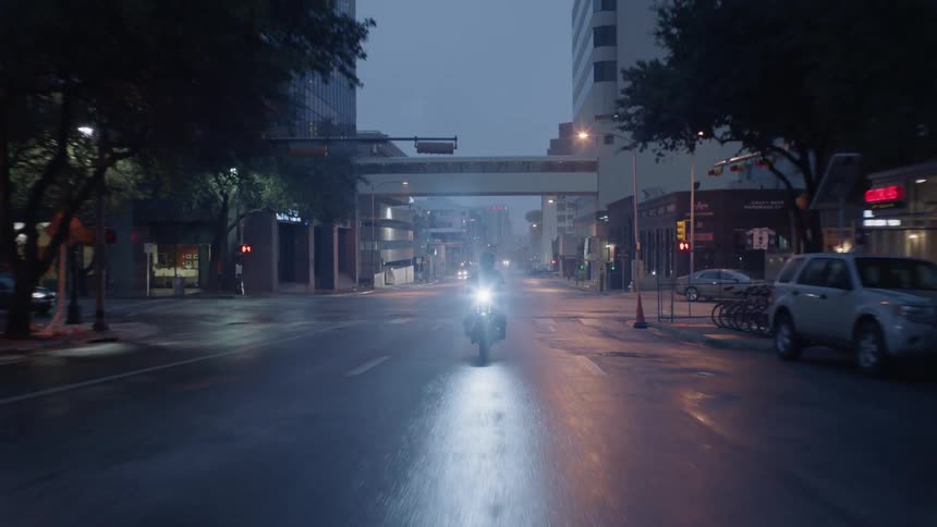 A man is riding a motorcycle on a city street at dusk