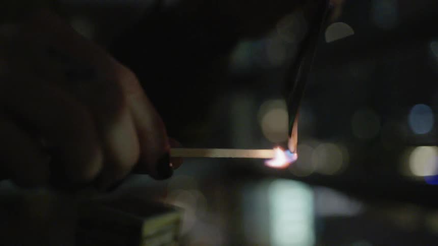 A woman burns a photograph she is holding with a lit match