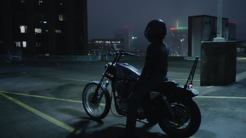 A woman sits on a motorcycle on top of a parking garage