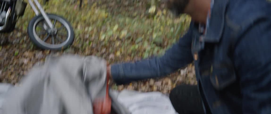 A man is unfolding a tent on the ground in a wooded area during the day