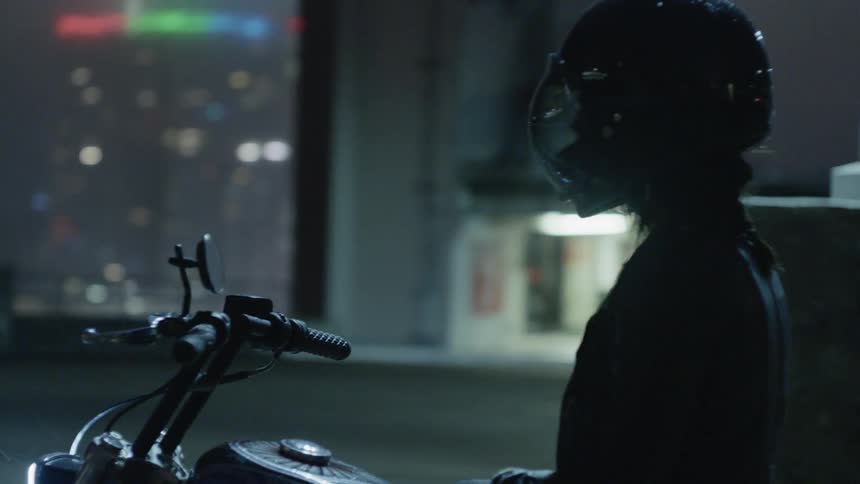 Person wearing a helmet sits on a motorcycle in a city at night