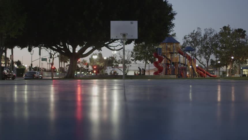 A child skips onto an empty basketball court while other play on the playground