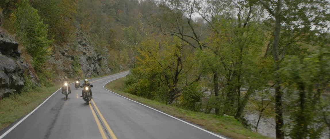 A group of motorcyclists are riding on a road near a river during the day