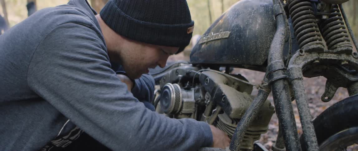 A man attempts to insert a dollar bill into a motorcycle engine