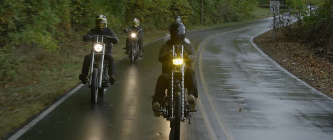 Motorcyclists riding a paved road on a wet day