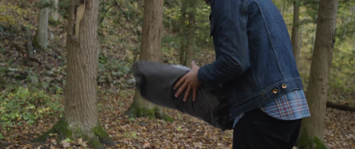 A man unfurls a tent in the woods