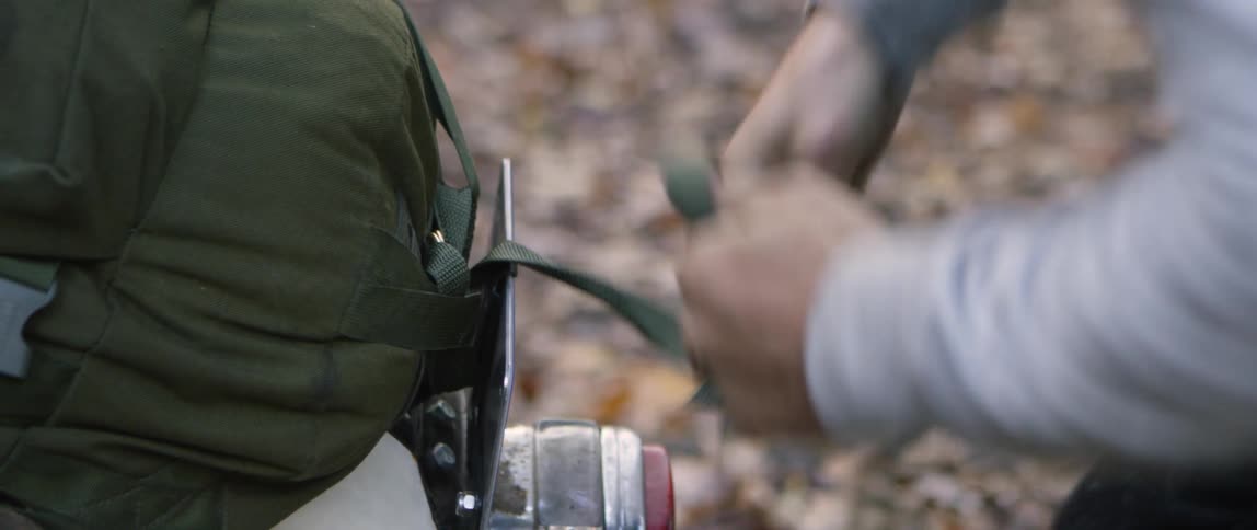 Person fastens a backpack outside in the woods