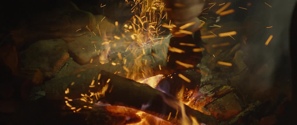 A person adds logs to a campfire at night