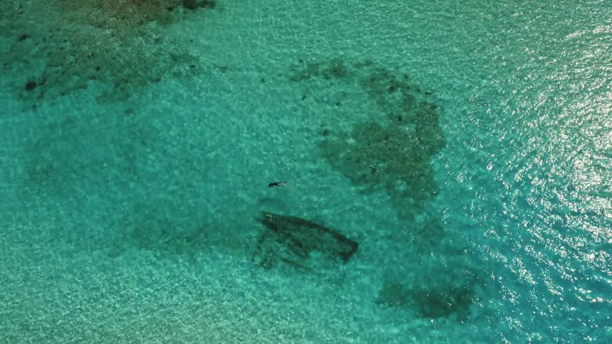 The outline of a sunken boat can be seen under the water