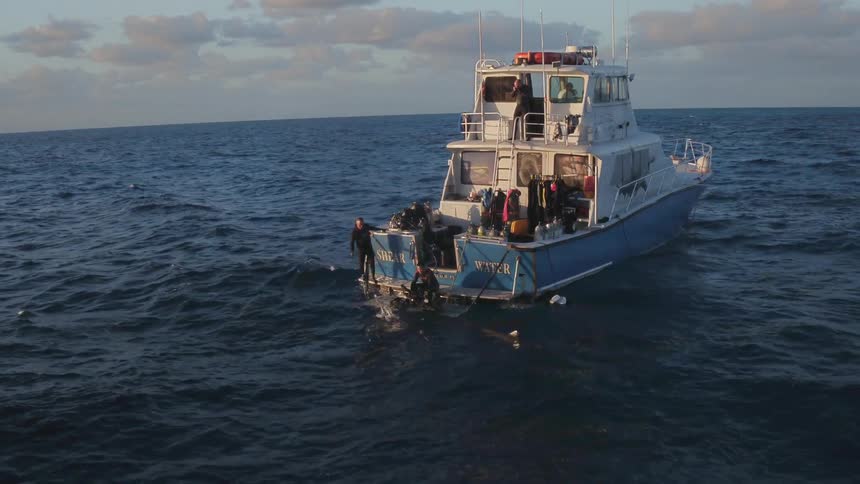 A large boat is rocking in the waters with people sitting on the edge