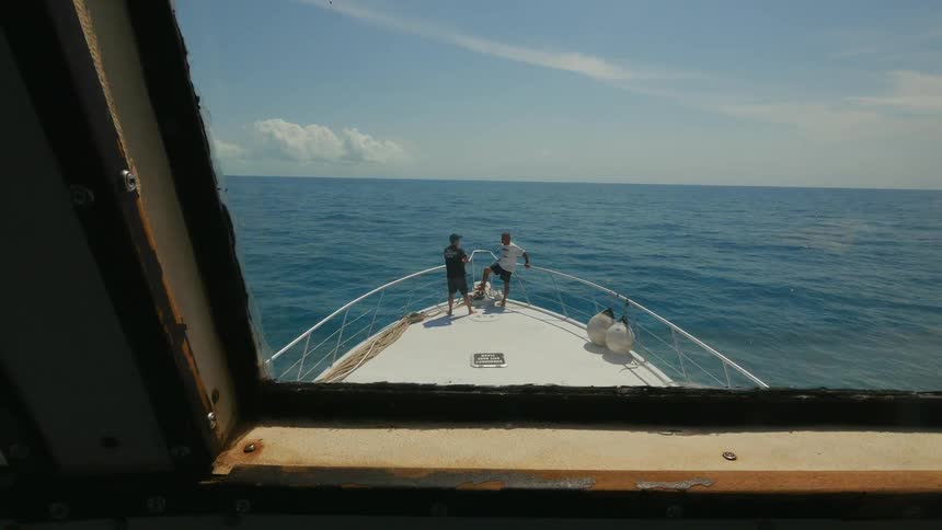 Two men stand on the deck of a boat as it sails on the ocean