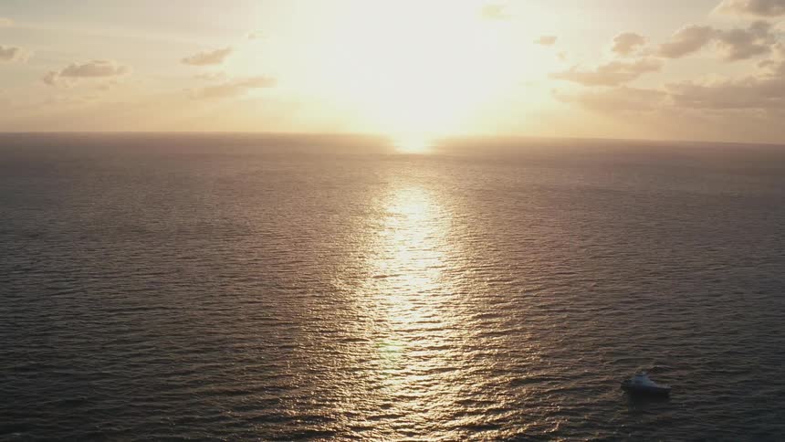 A boat is floating in the ocean at sunset