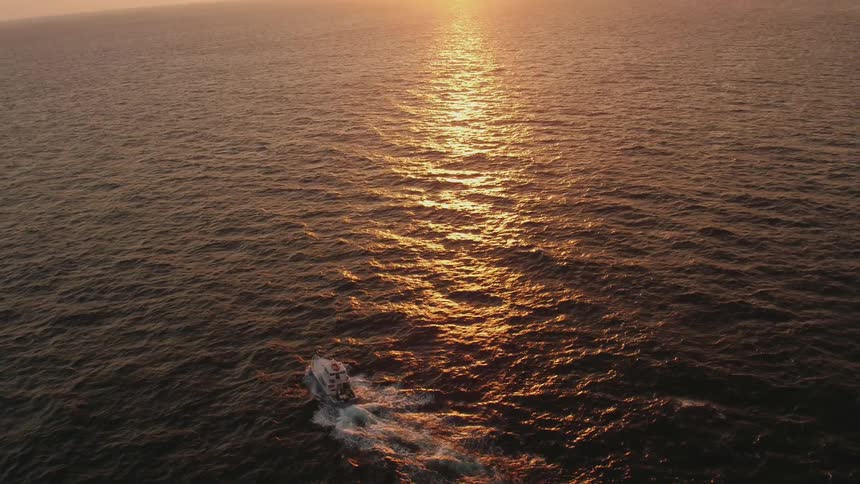 A boat is making its way through some choppy seas at sunset