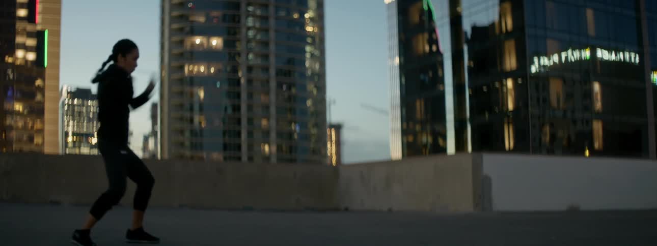 A female athlete is shadow boxing on a rooftop in a city at dusk